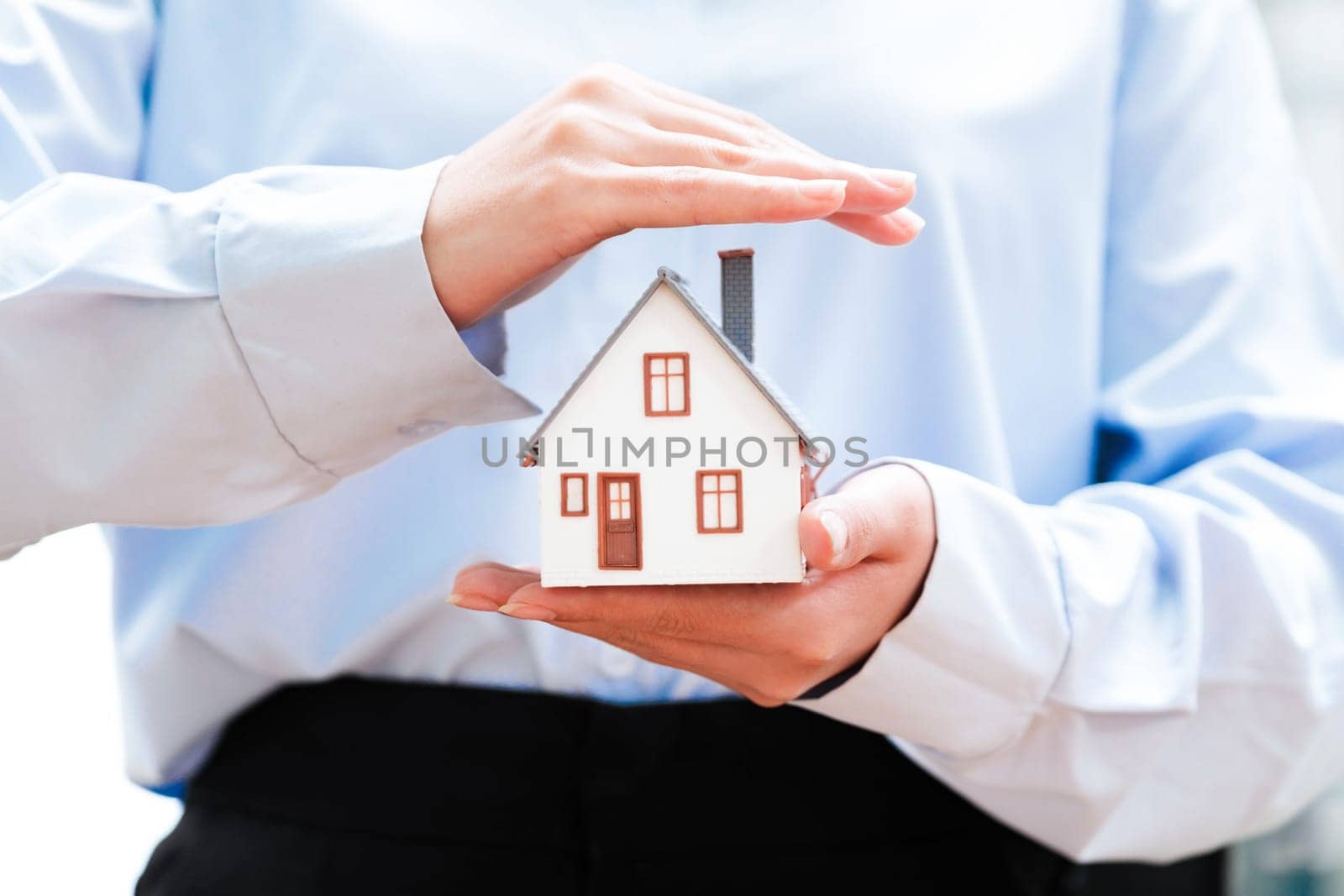 Hands holding a small house model, depicting safety and security in homeownership. by ijeab