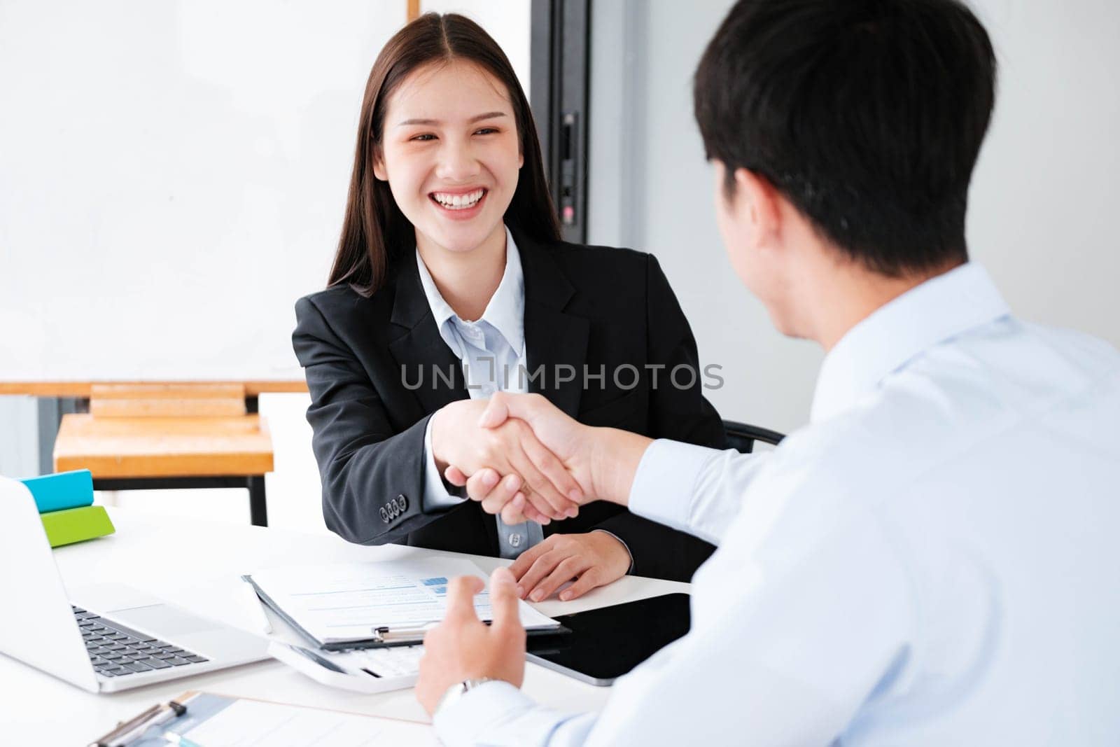 A young businesswoman smiles while shaking hands, making a positive impression during a professional meeting.