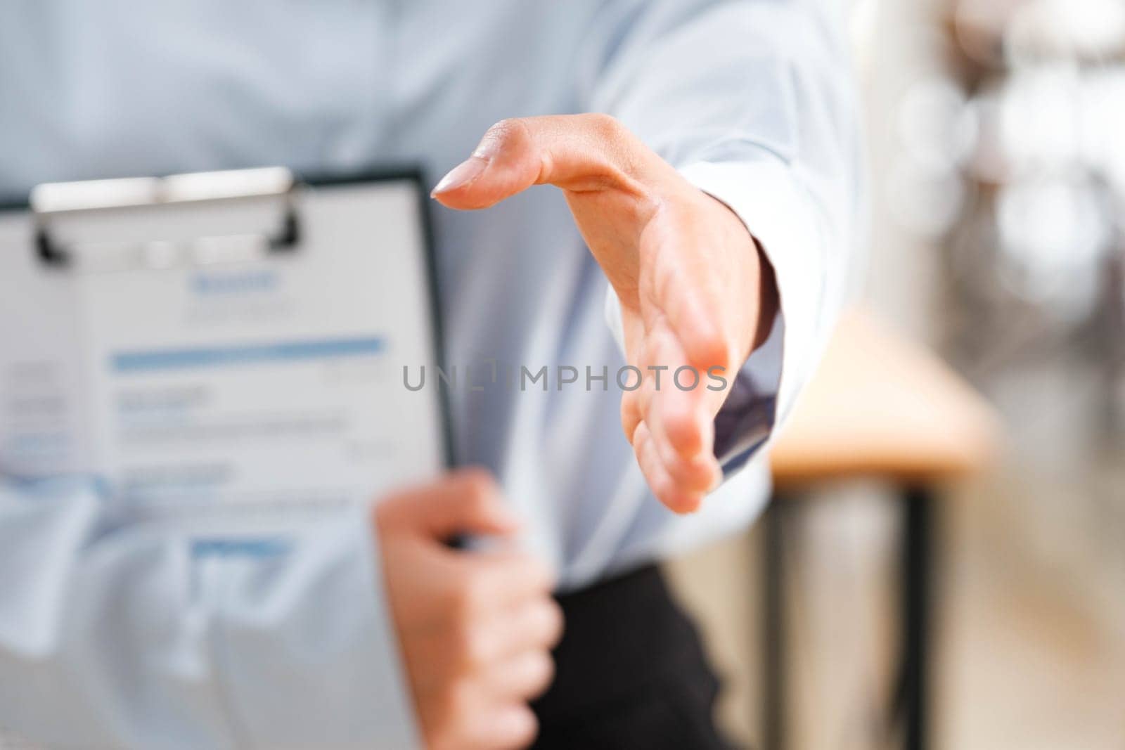 Business Professional Extending Hand for a Handshake, Gesture of Introduction or Agreement with Clipboard in Background