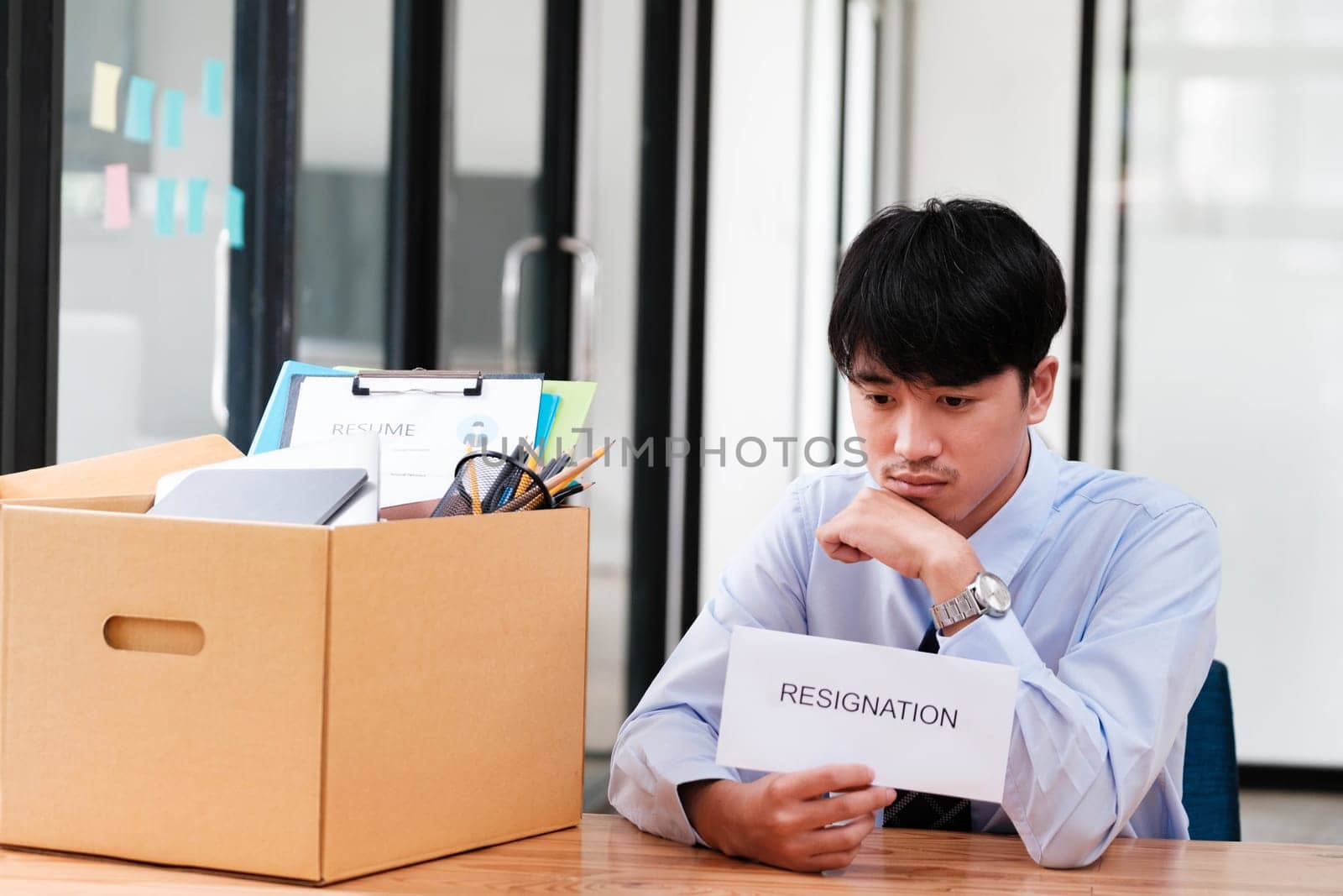 Man at desk with resignation letter, pondering his decision beside a packed box. by ijeab