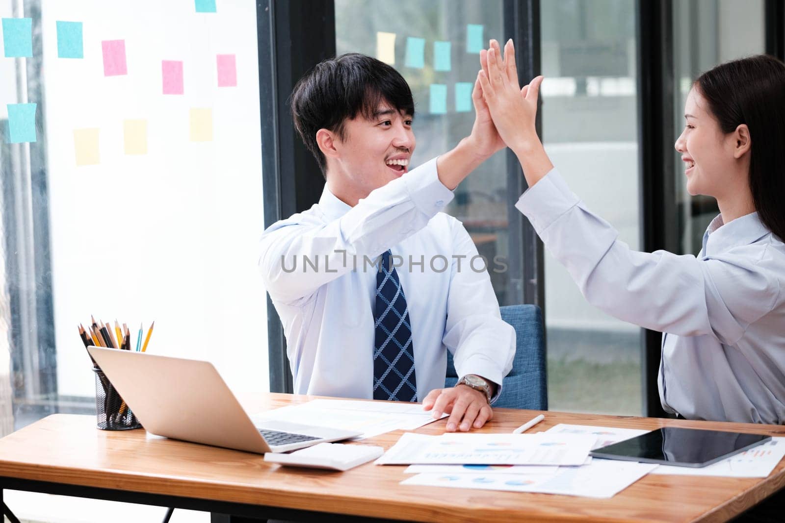 Two elated business colleagues giving a high-five over a successful project at their office workspace.