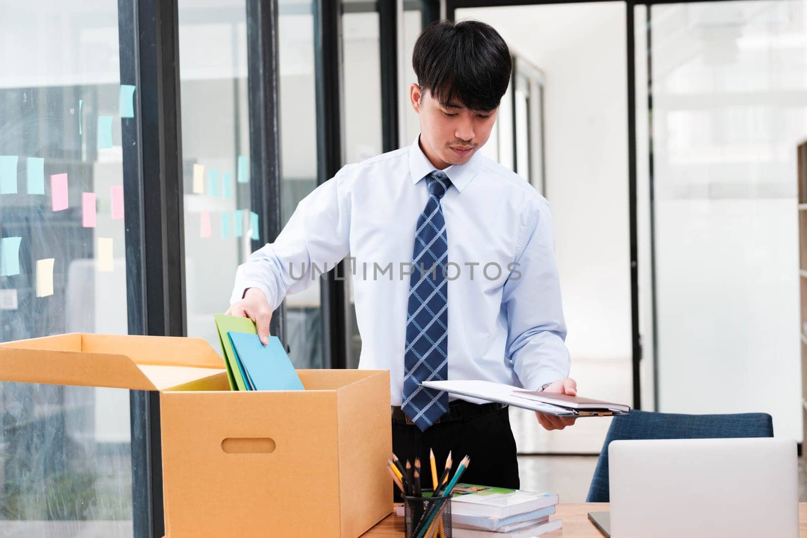 A man in a suit is opening a cardboard box on a desk. The box contains papers and a laptop