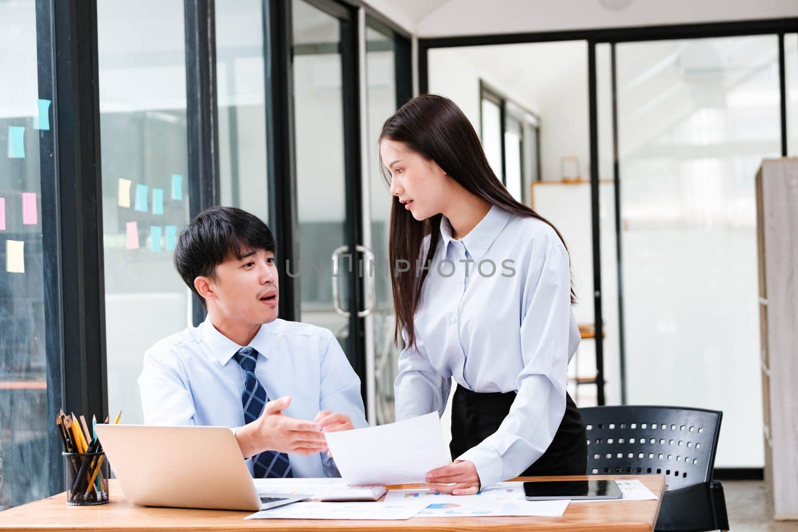 Asian business colleagues in discussion over digital and paper data analysis for company growth strategy at an office desk.