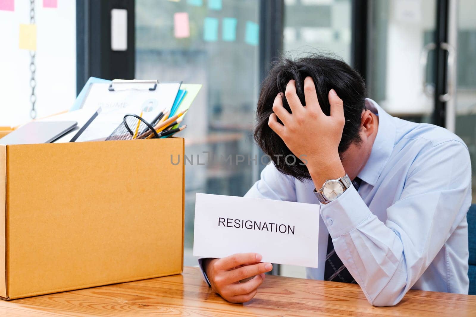 Contemplative Man at Office Desk with Packed Box and Resignation Letter, Reflecting on Career Change and Next Steps