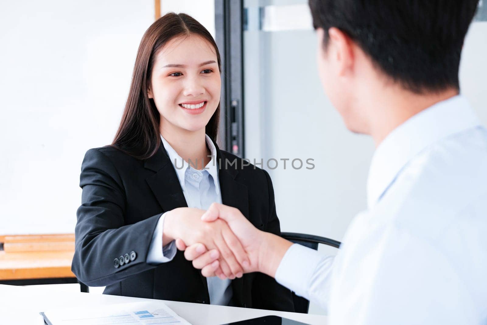 A young businesswoman smiles while shaking hands, making a positive impression during a professional meeting.