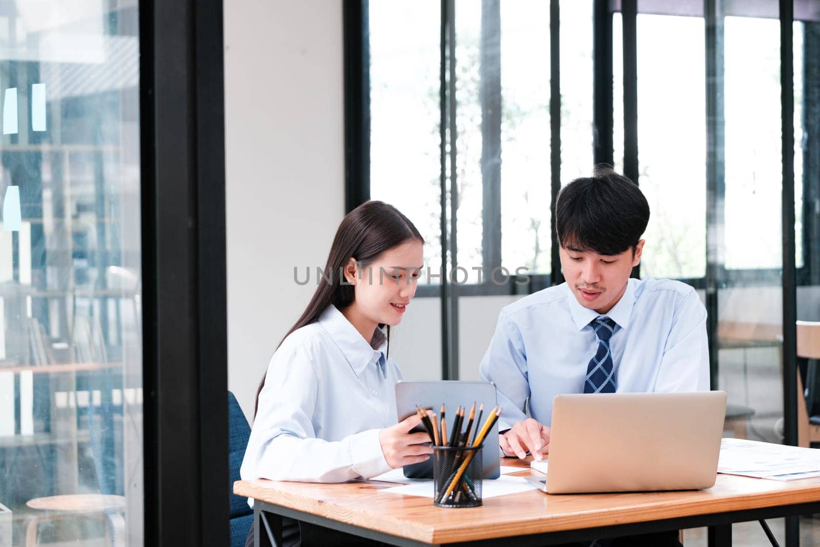 Two professional colleagues discussing paperwork and digital content on a laptop in a modern office setting.