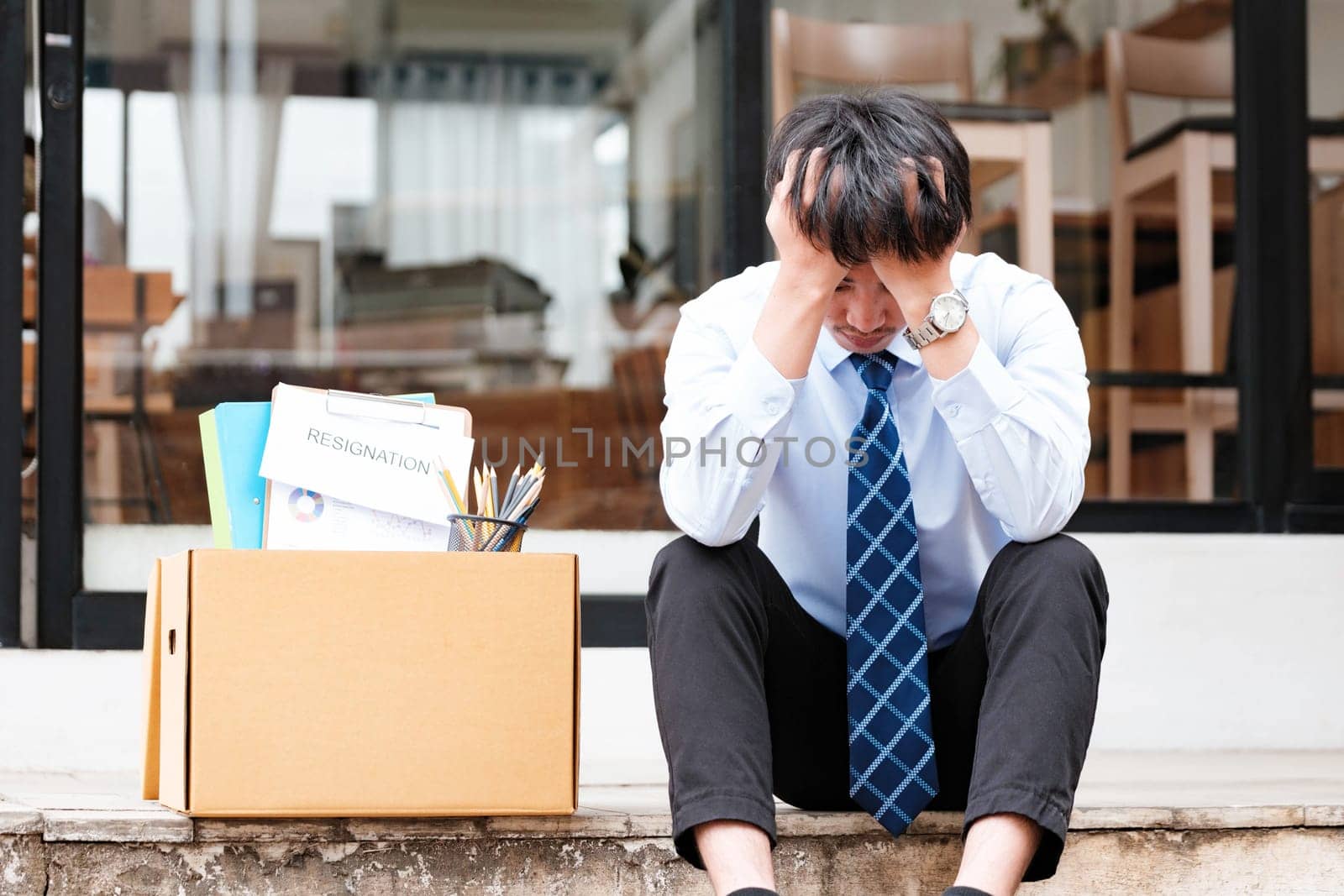 Disheartened Man Sitting on Stairs with Box of Personal Items, Overwhelmed by Emotions After Resignation or Job Loss