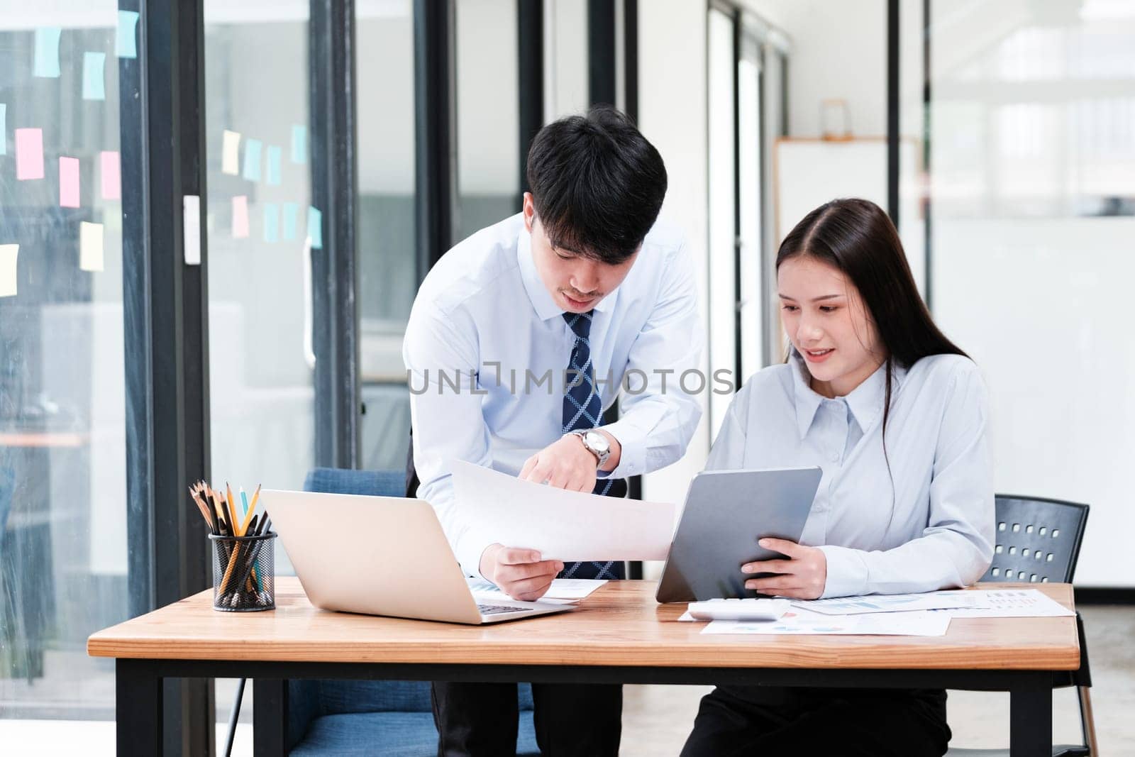 Asian business colleagues in discussion over digital and paper data analysis for company growth strategy at an office desk.