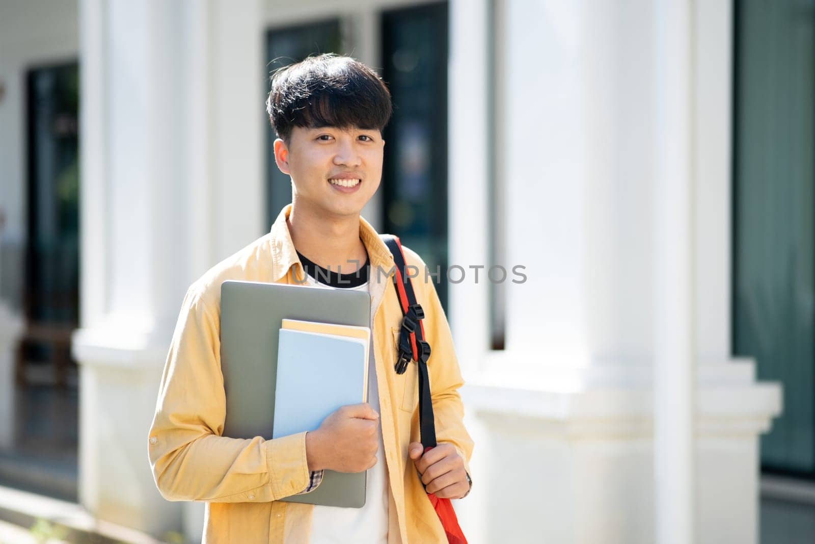 A contented college student carrying a laptop and books walks across the campus grounds, exuding a sense of readiness and enthusiasm for learning.