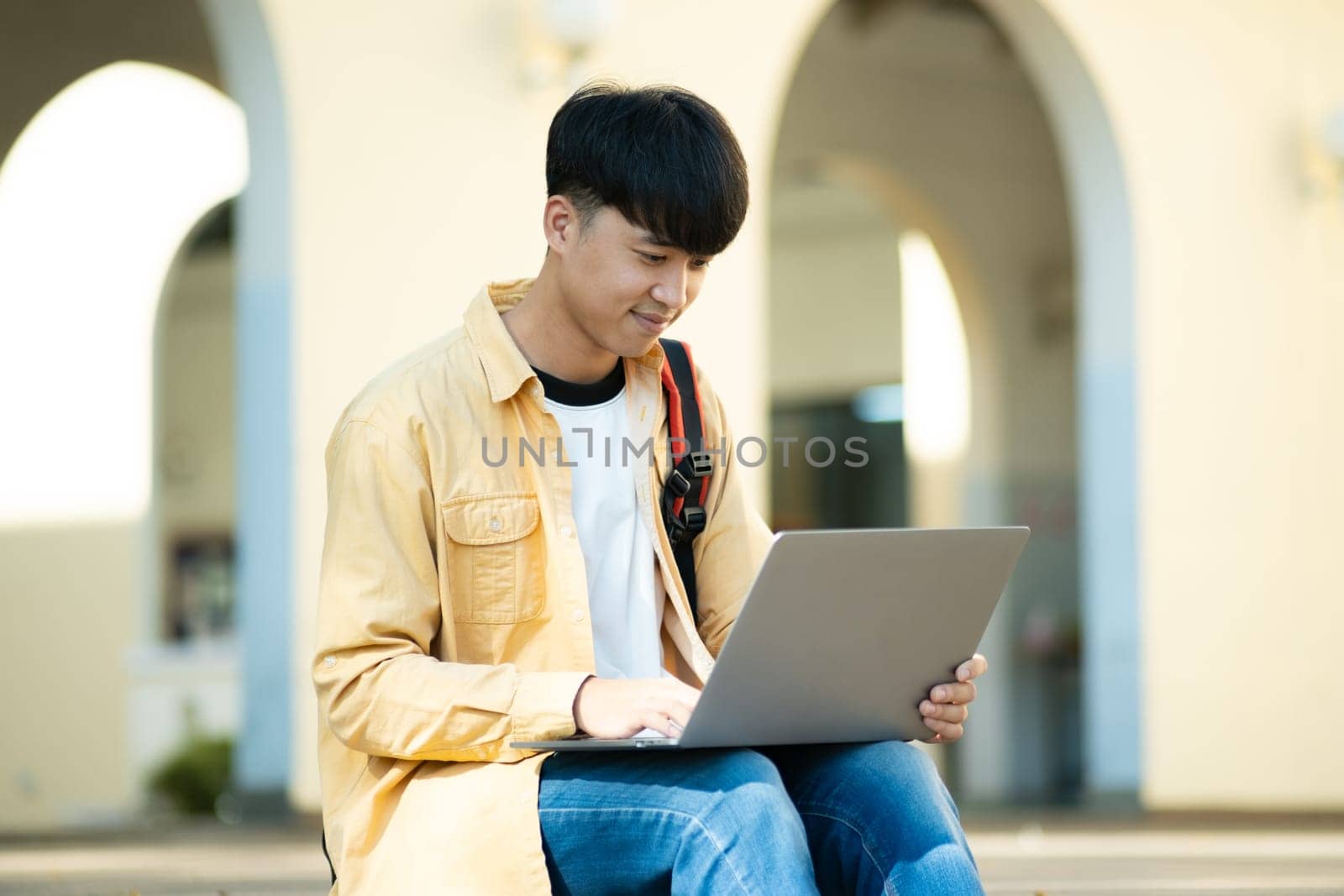 Pensive Student with Laptop Outdoors on University Grounds by ijeab