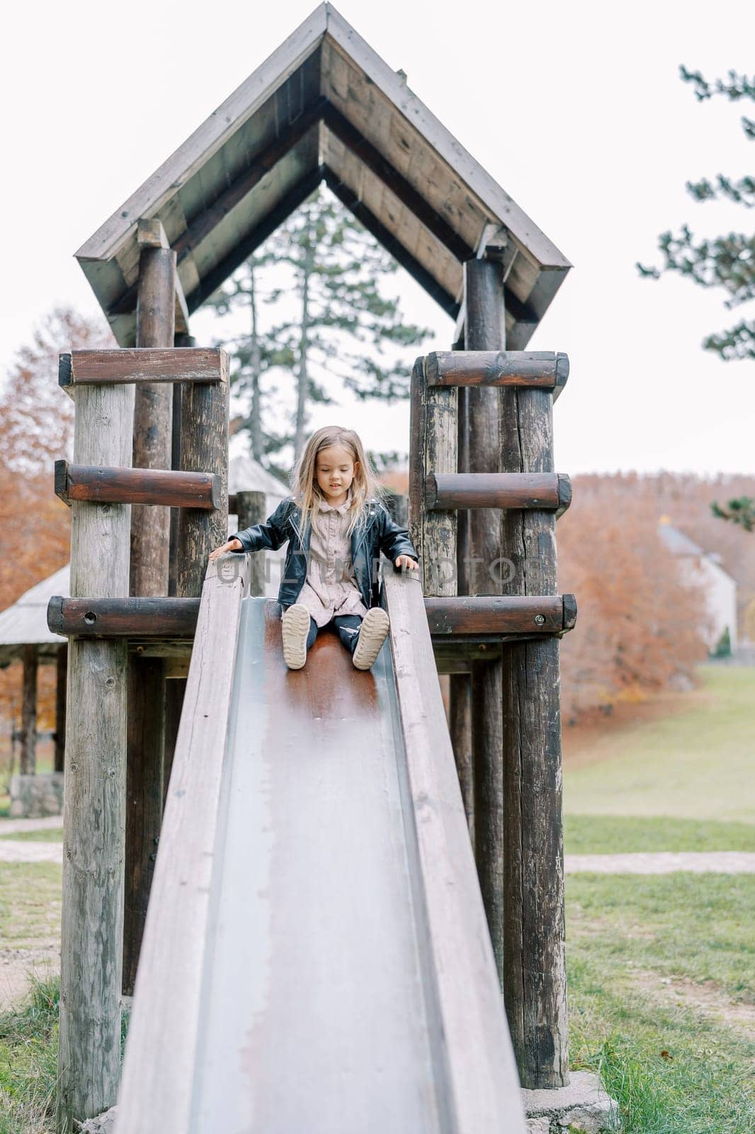 Little girl going down a wooden slide on a playground in a park. High quality photo