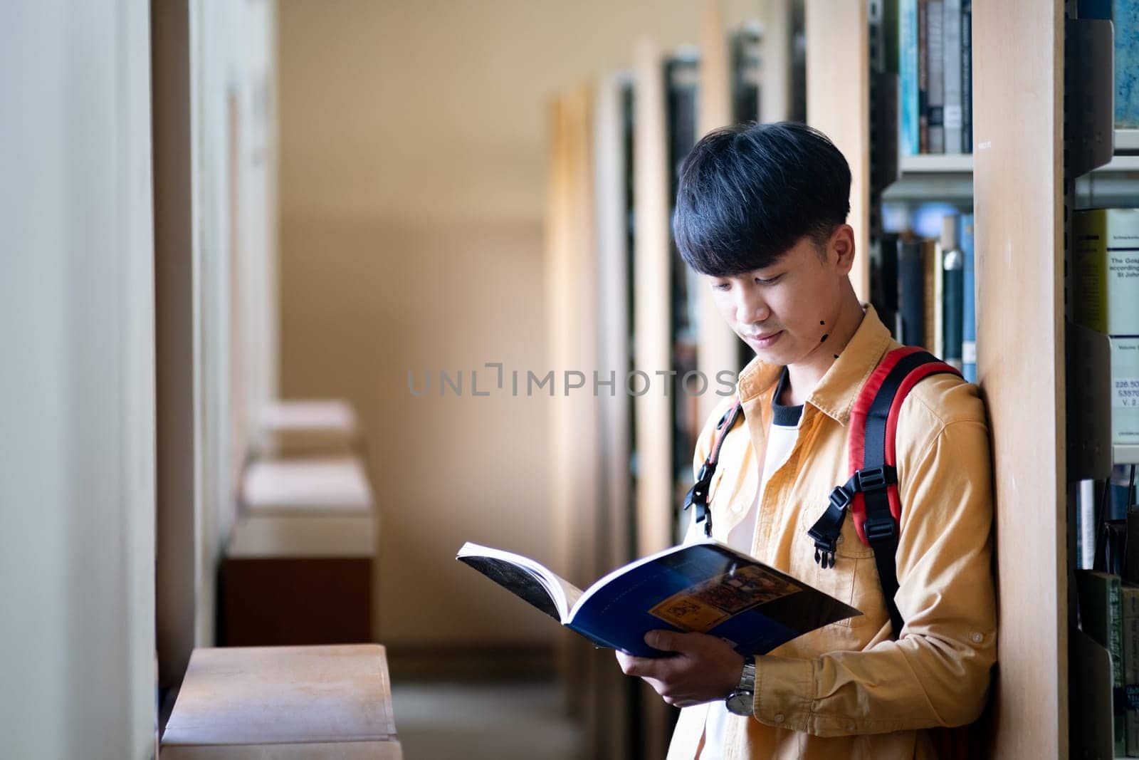 A young man is reading a book in a library by ijeab