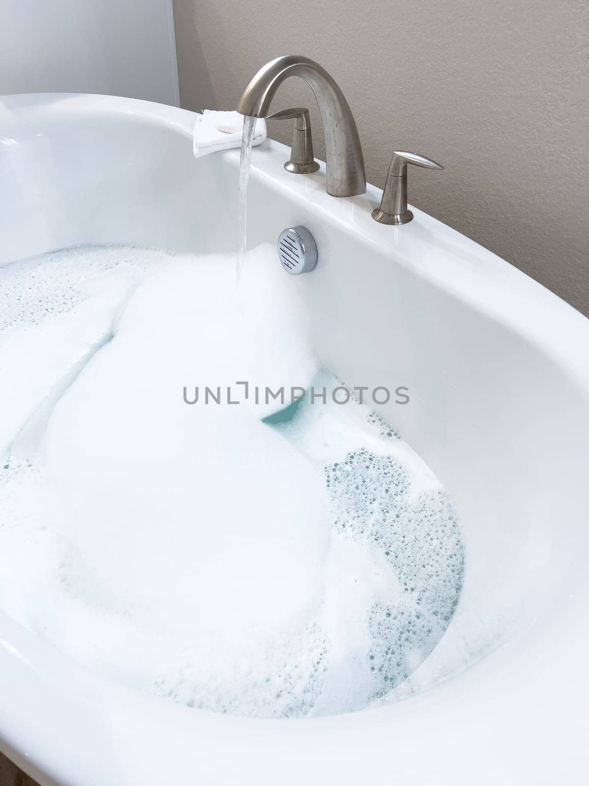 Elegant white bathtub filled with water, featuring a sleek brushed nickel faucet with water flowing gently into the tub. The bathtubs modern design and the clear, tranquil water suggest a peaceful bathroom setting.