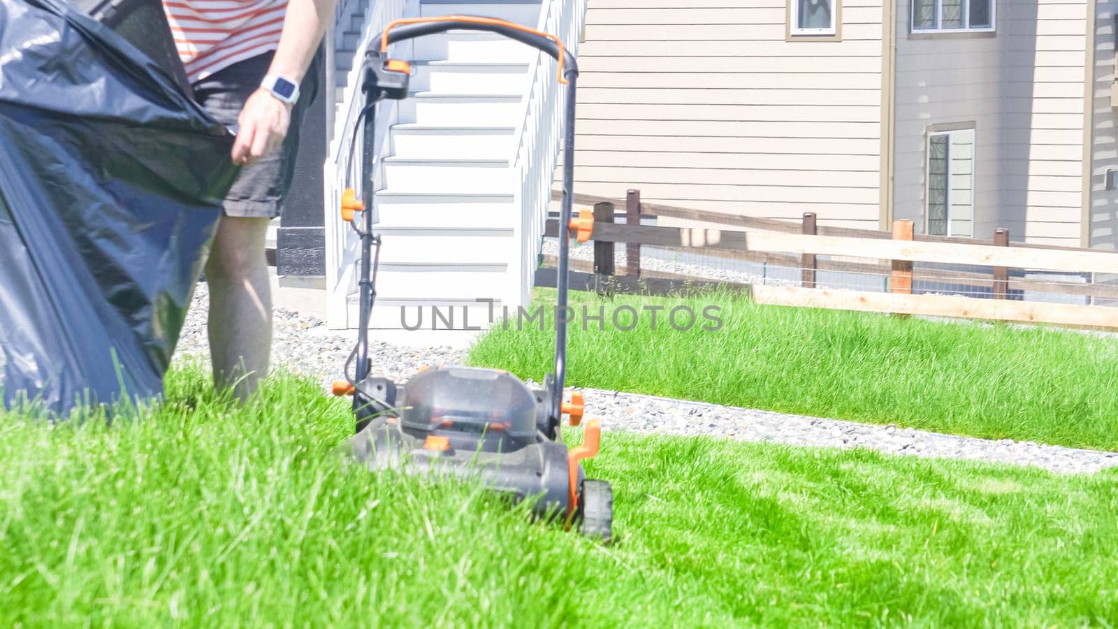 At a residential suburban house, a lush green lawn is meticulously mowed using an electric lawn mower, creating a well-manicured and inviting outdoor space.