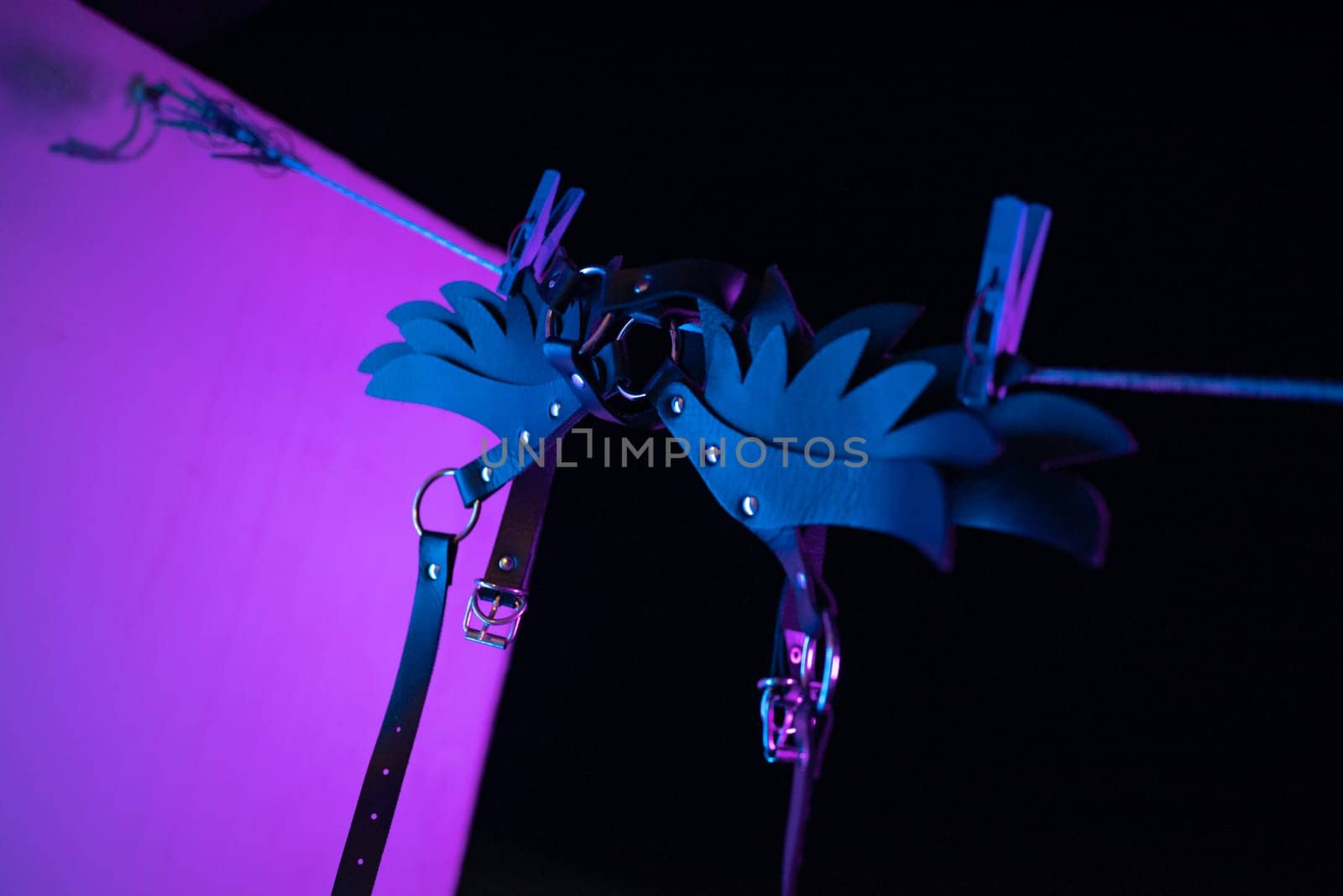 bdsm leather shoulder straps in the shape of wings hanging on clothesline in neon light on a black background, conceptual photos