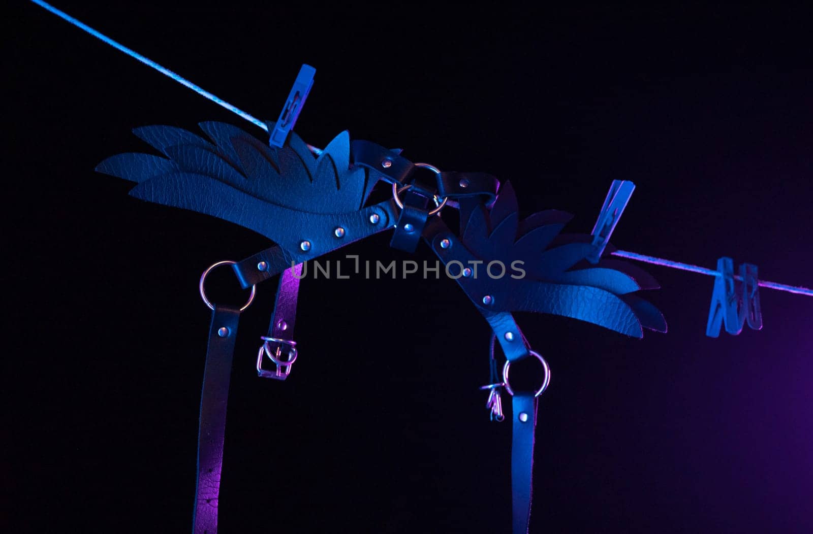 bdsm leather shoulder straps in the shape of wings hanging on clothesline in neon light on a black background, conceptual photos