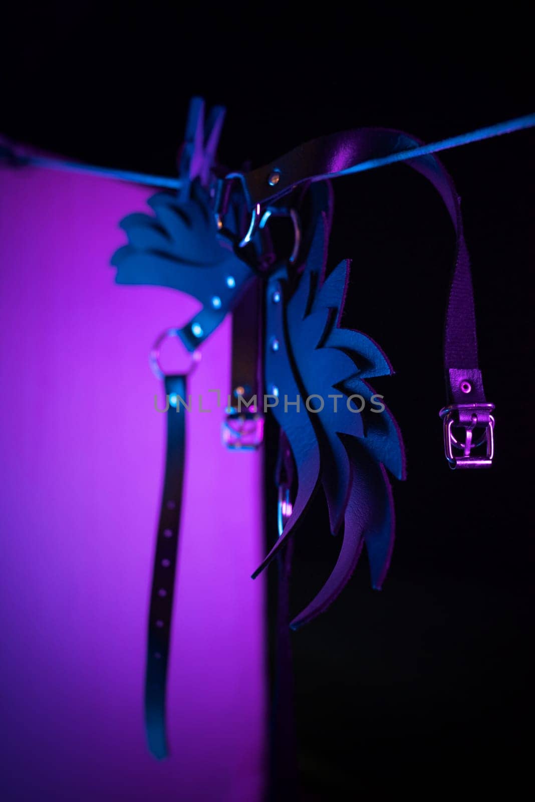 bdsm leather shoulder straps in the shape of wings hanging on a clothesline in neon light on a black background, conceptual photos by Rotozey