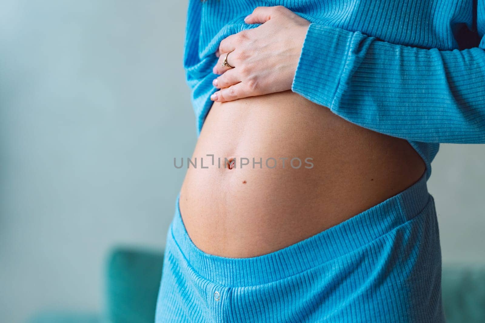 Close-up of young pregnant woman touching her belly on 6th month of pregnancy and caring about her health. Motherhood and baby expectation concept. High quality photo