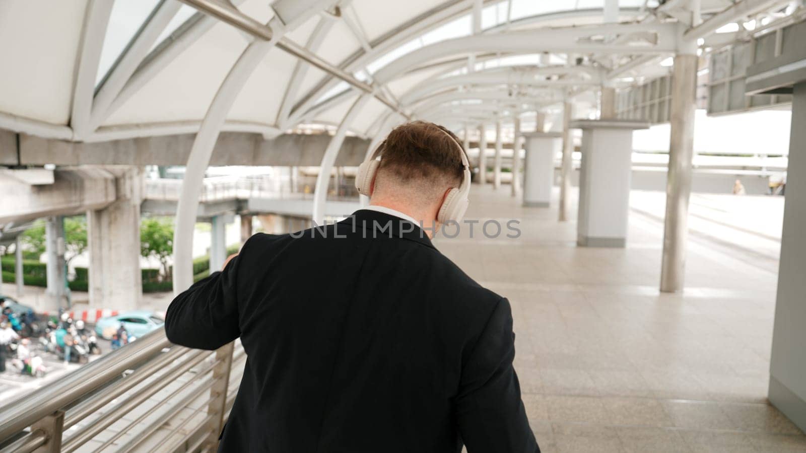 Happy business man dancing while wear headphone at bridge in urban city. Energetic manager motivation performance moving to music to celebrate successful project while walk along. Back view. Urbane.