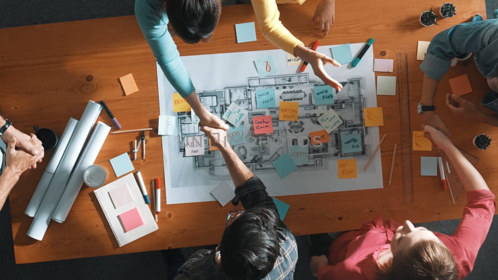 Top down view of smart business people shaking hands and making a contract. Aerial view of architect engineer working together and dealing plan or project at table with blueprint and notes. Symposium.