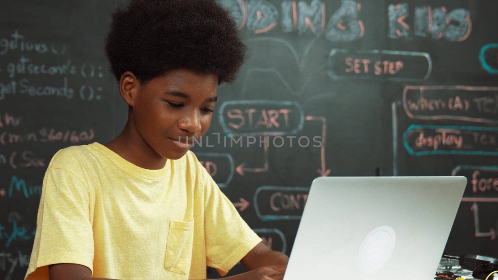 Smart african boy programing system or coding system by using laptop. Skilled highschool student working learning to write engineering code while sitting blackboard. Creative education. Edification.