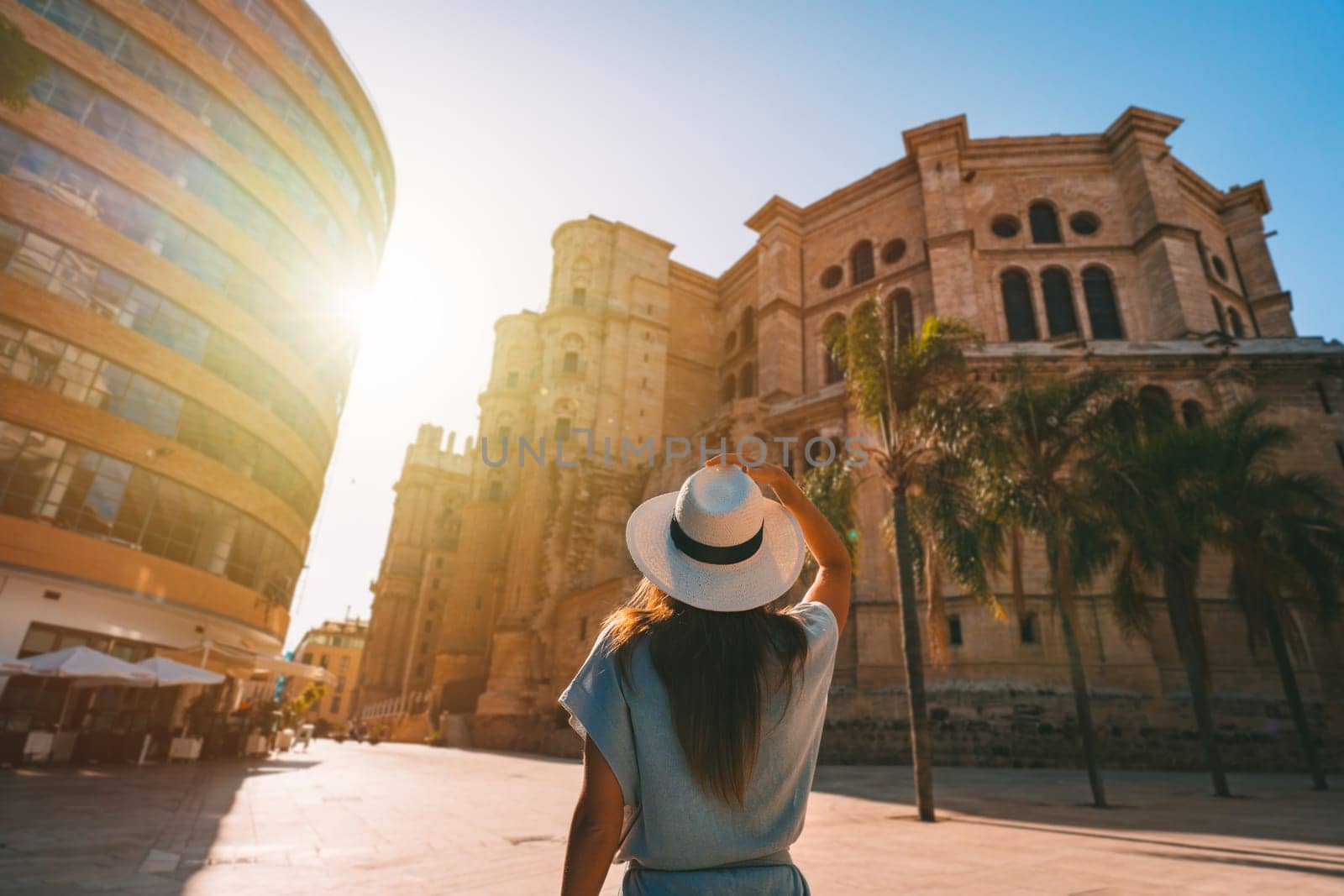 Rear view of young tourist woman in white sun hat walking in Malaga city at sunset. Summer holiday vacation in Spain. High quality photo