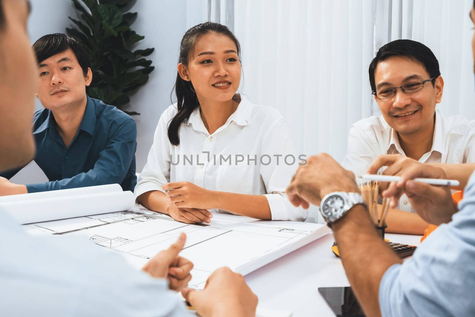 Diverse group of civil engineer and client working together on architectural project, reviewing construction plan and building blueprint at meeting table. Prudent