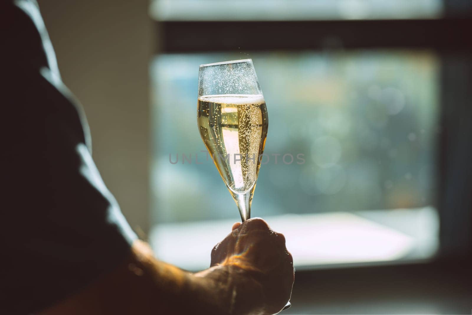 A photo of a hand holding a glass of champagne with bubbles on sunset light. Celebration or holiday concept.High quality photo