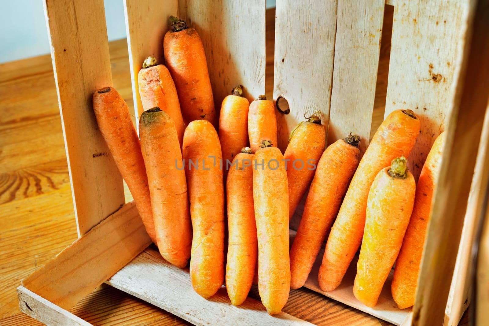 Bunch of orange carrots in wooden box on wooden table ready for cooking or selling