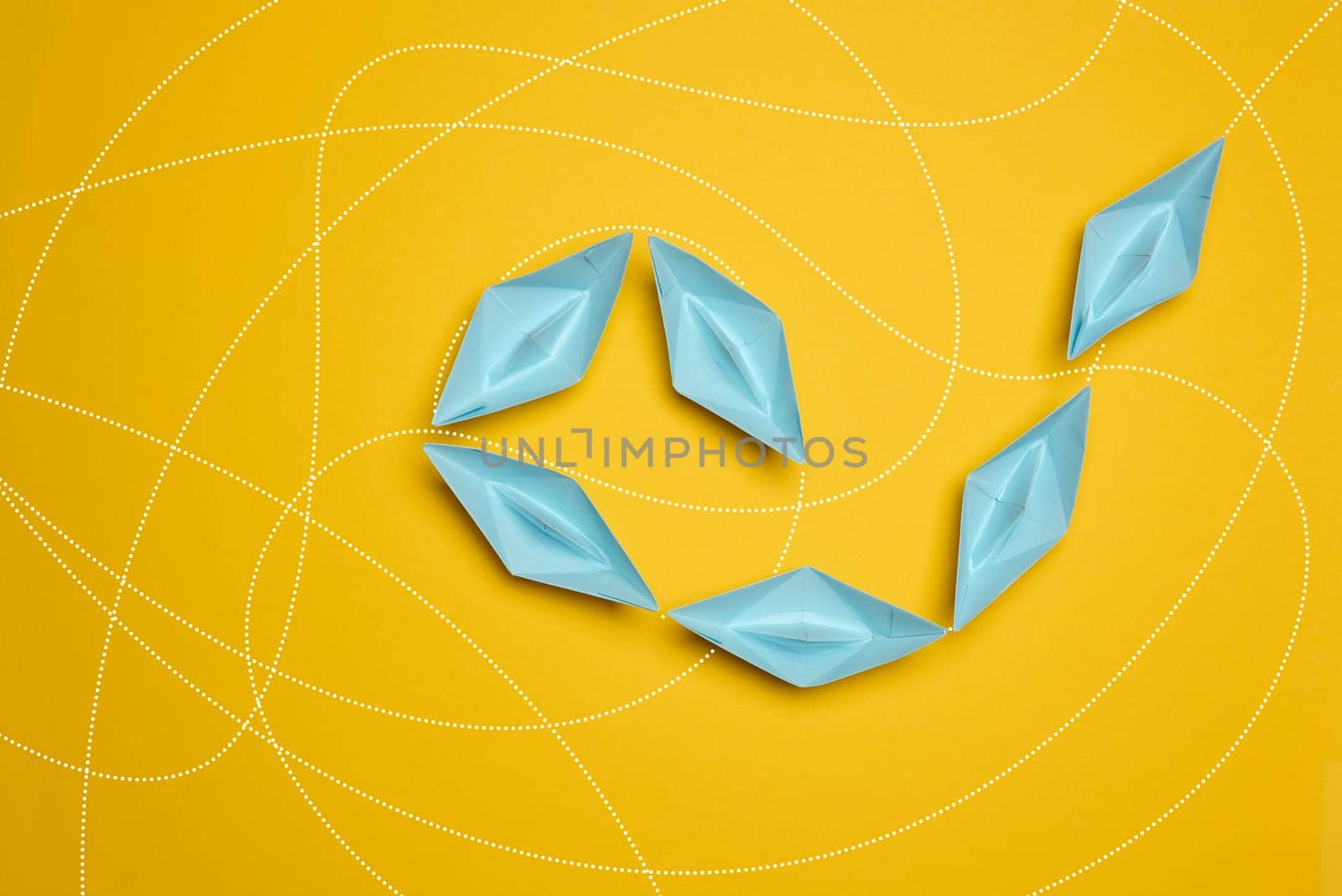 Blue paper boats move one after another on a yellow background, top view