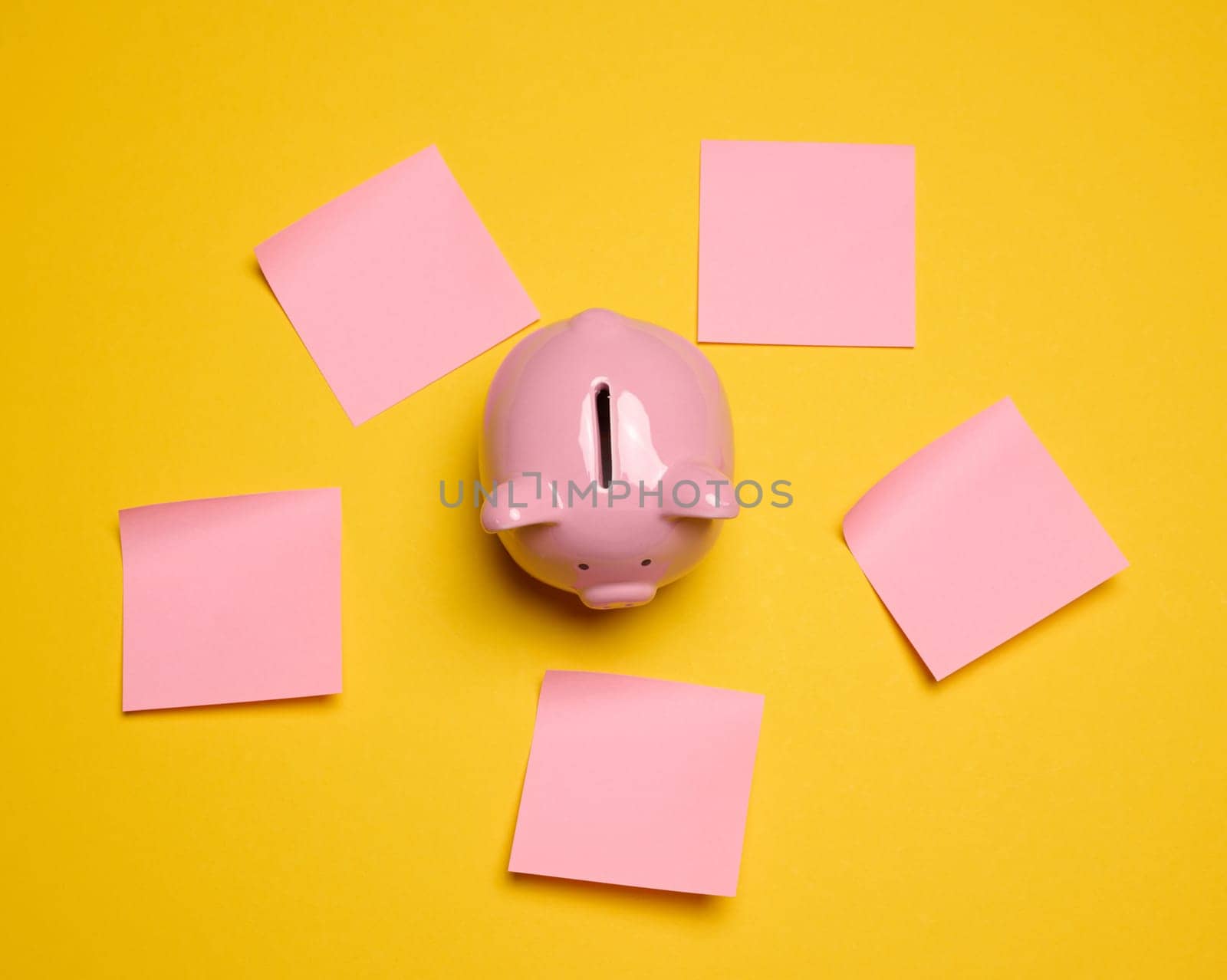 Pink ceramic piggy bank and paper stickers on a yellow background by ndanko