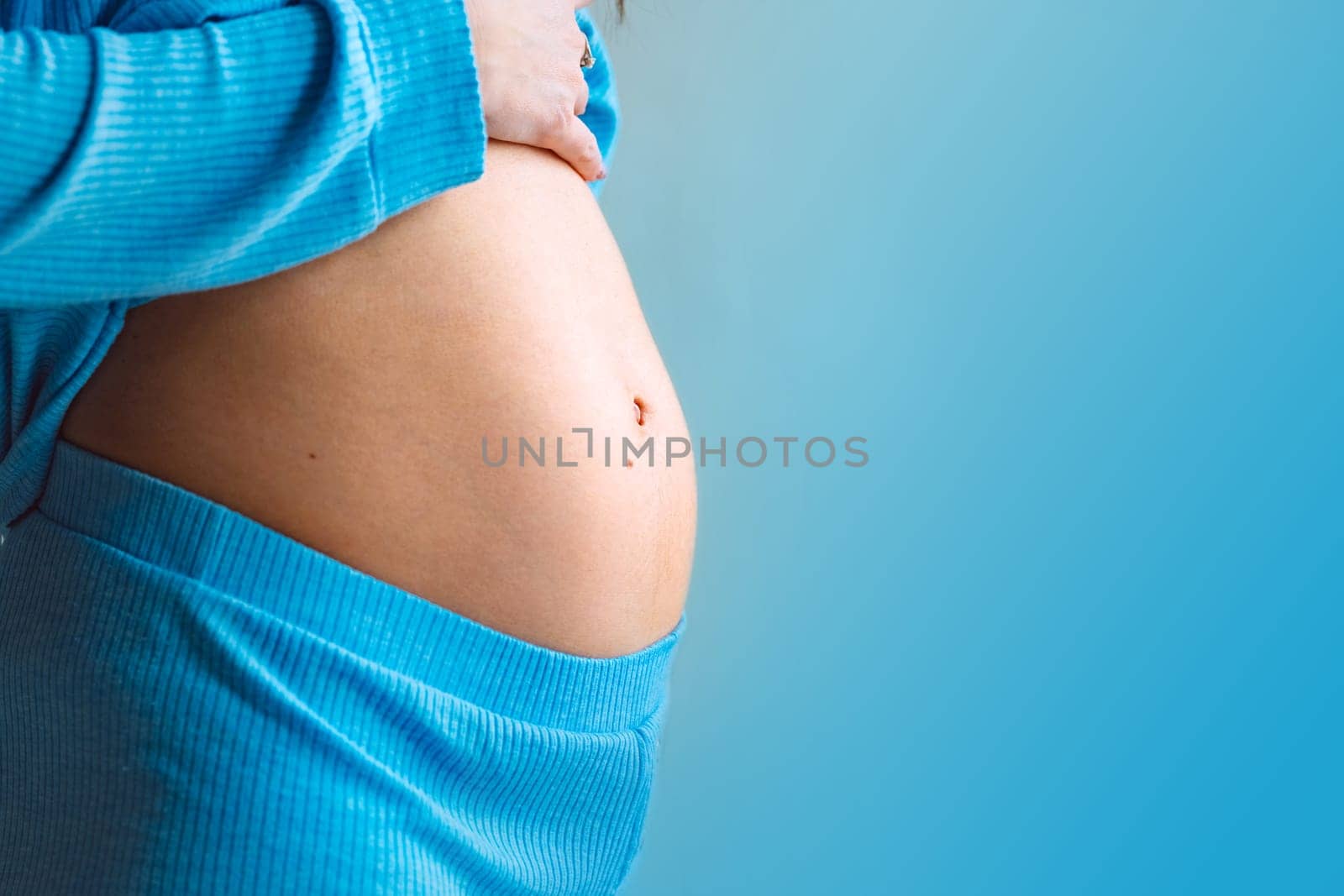 Close-up of young pregnant woman's belly on blue color background. Motherhood and baby expectation concept by DariaKulkova