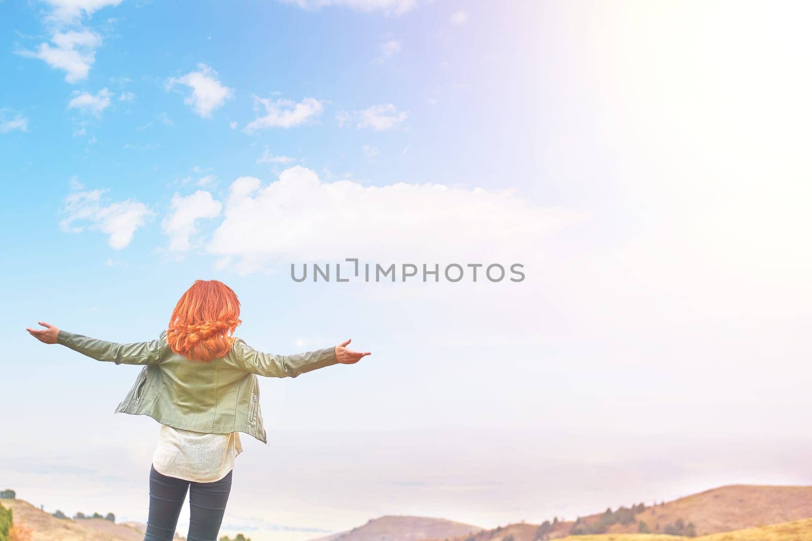 Woman in the mountain standing in the distance with her back to the camera and her arms outspread in celebration of a beautiful sunny summer day and freedom.