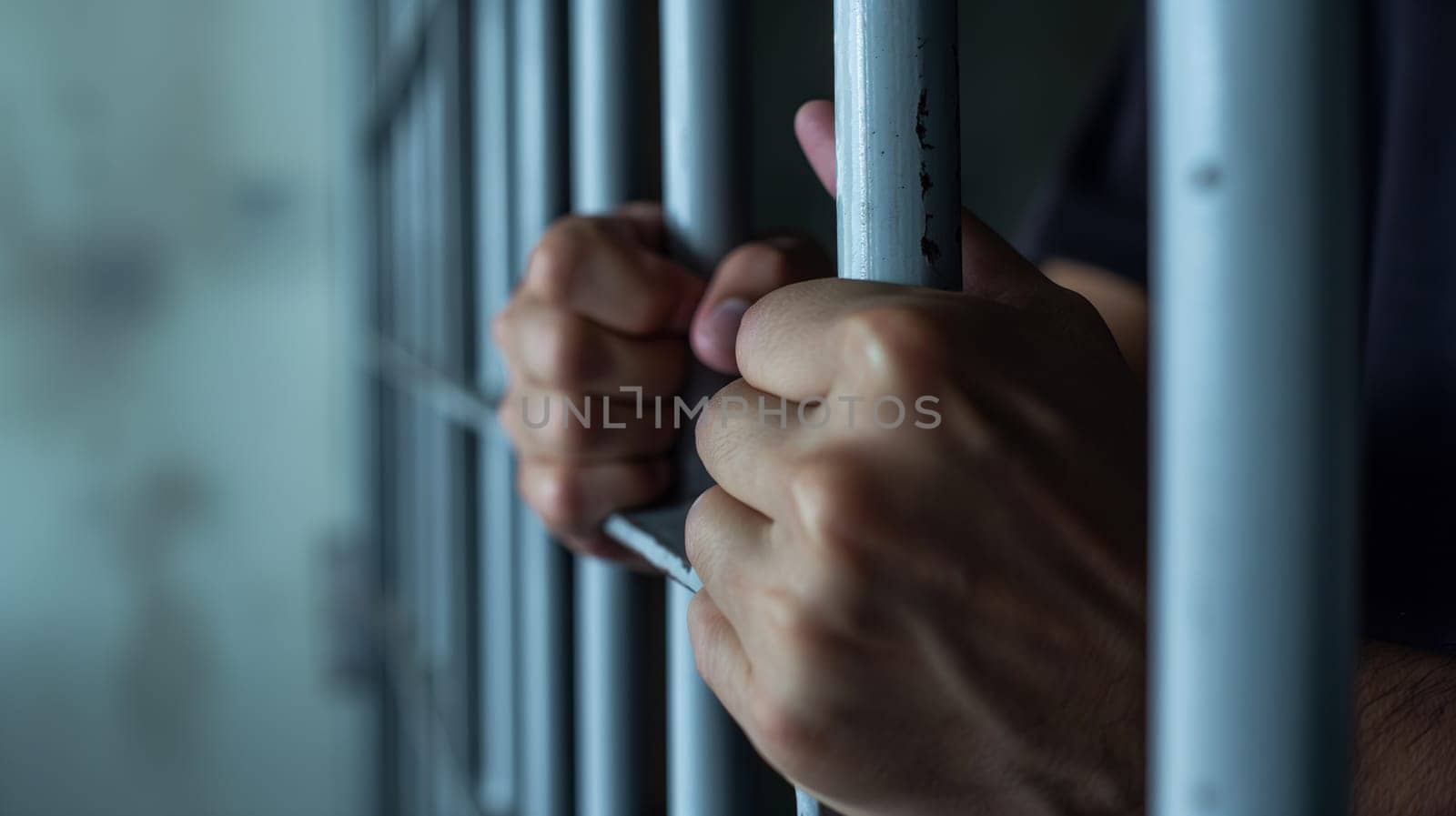 Hands Clasping Jail Bars in a Dimly Lit Cell by chrisroll