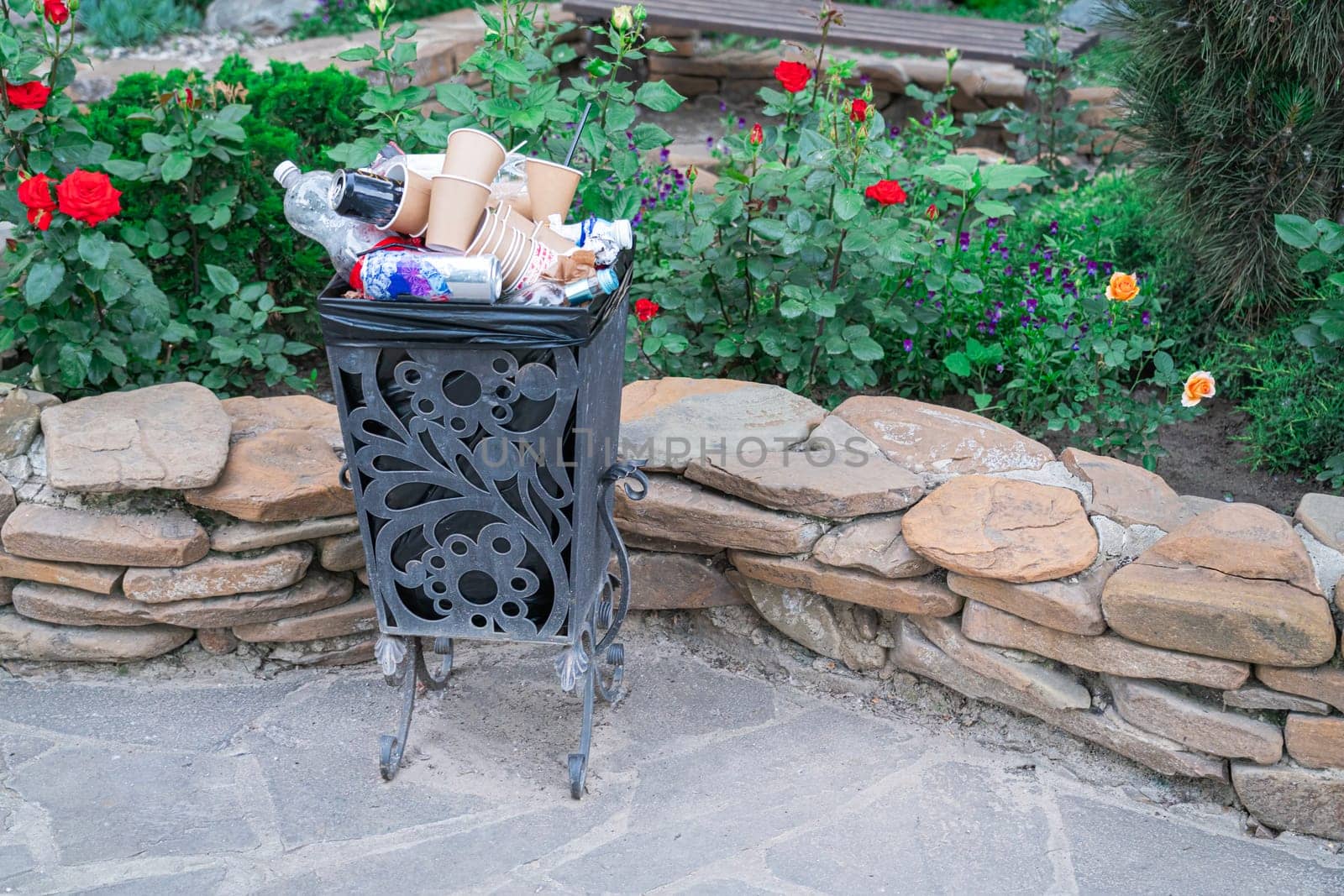 a filled trash can in the park on a background of flowers. photo