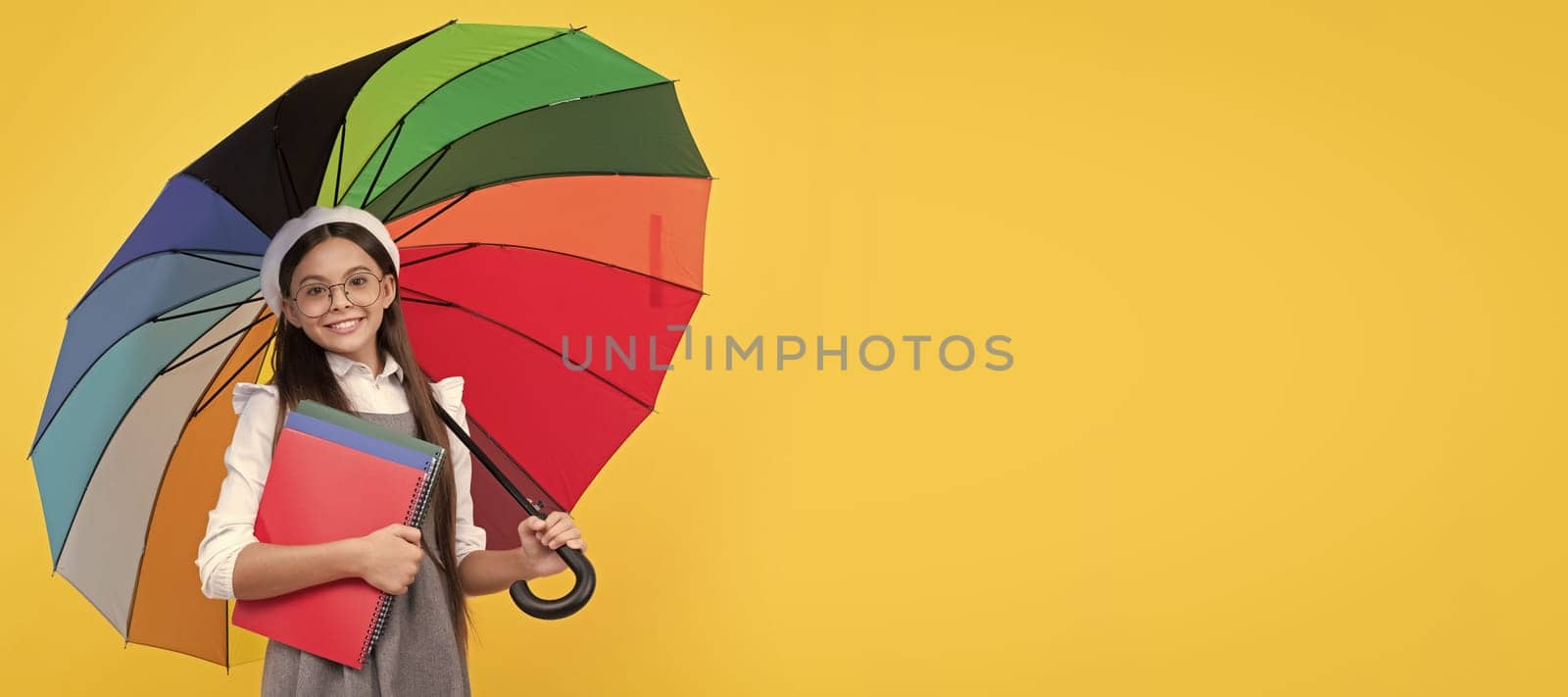 happy teen girl under colorful umbrella for rain protection in autumn season hold notebook. Child with autumn umbrella, rainy weather, horizontal poster, banner with copy space. by RedFoxStudio
