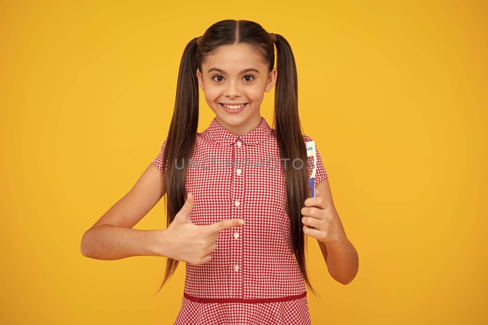 Girl cleans her teeth with a brush. Portrait beautiful teen holding toothbrush brushing teeth isolated on yellow background, Dental health concept. Happy teenager, positive and smiling emotions.