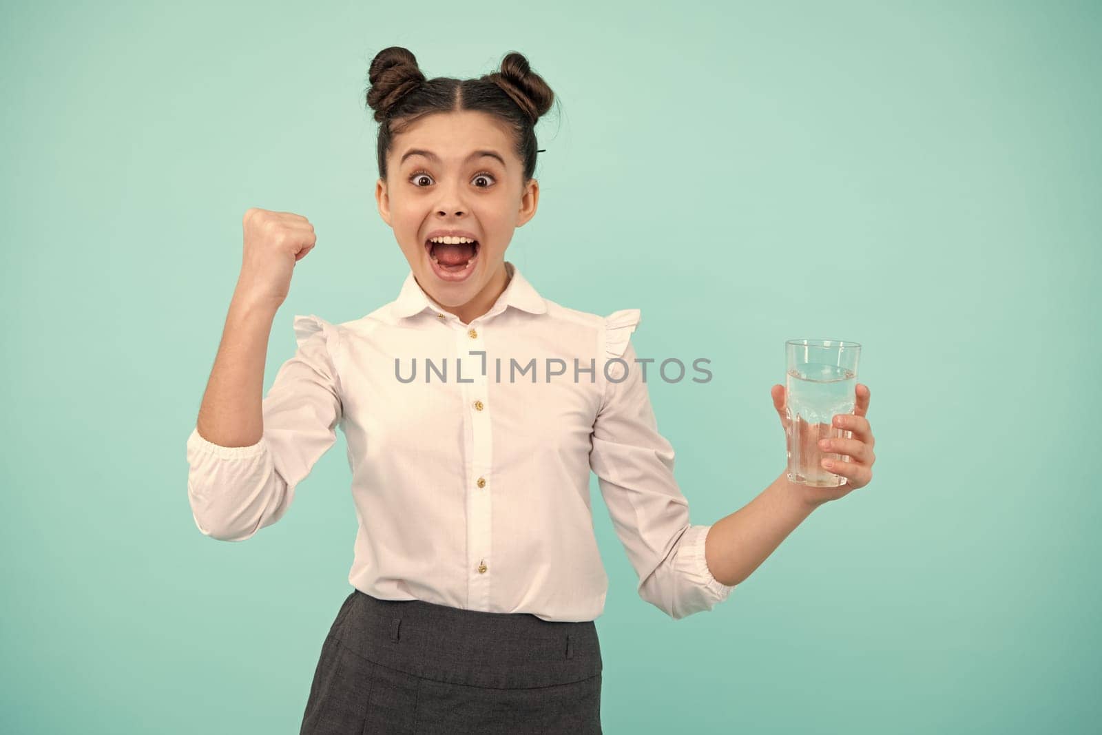 Amazed teenager. Cute teen girl drinking water from glass on blue background. Excited teen girl