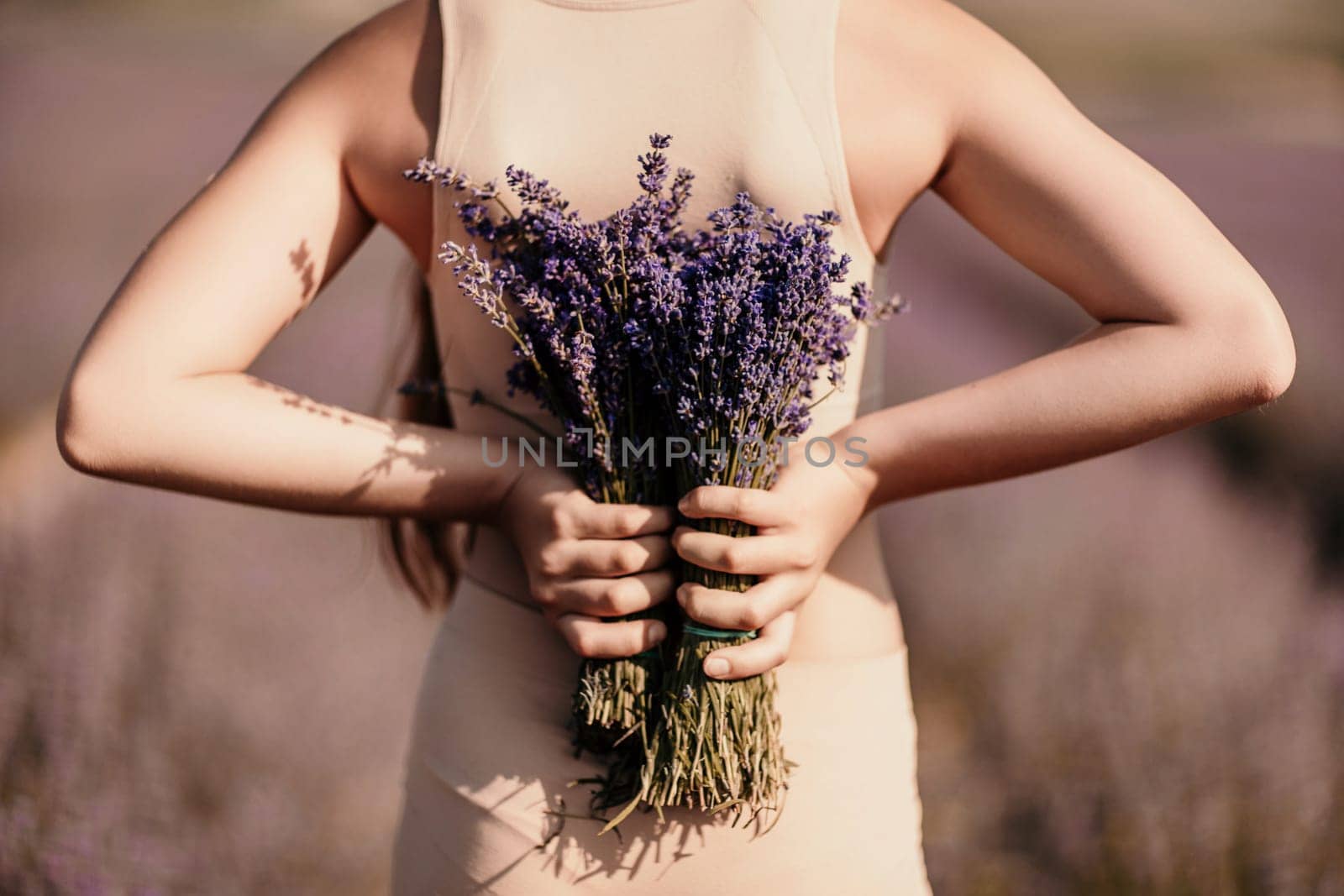 girl holding bouquet lavender flowers. The flowers are purple and the woman is wearing a tan top. Concept of calm and relaxation, as lavender is often associated with these feelings