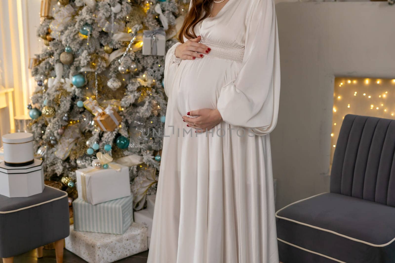 Pregnant woman holding a belly against Christmas tree with lights. family holiday concept. by Matiunina