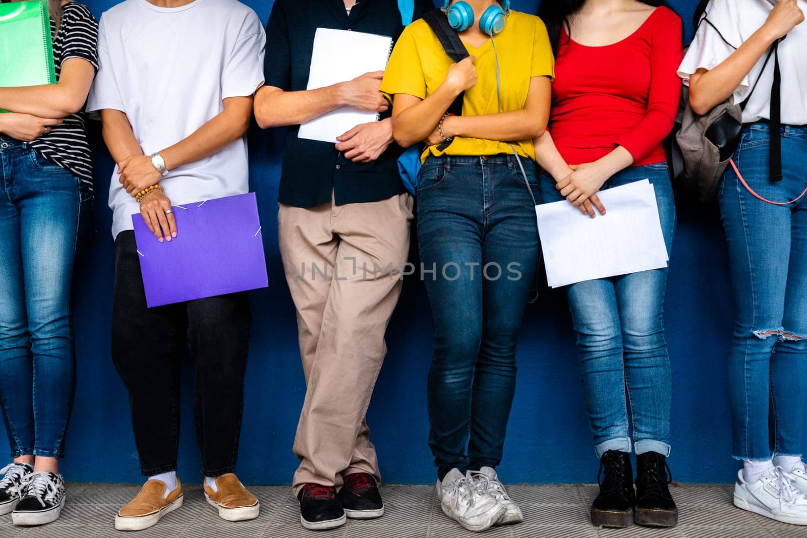 Small group of high school students stand leaning against blue wall before class. Back to school concept. Education concept.