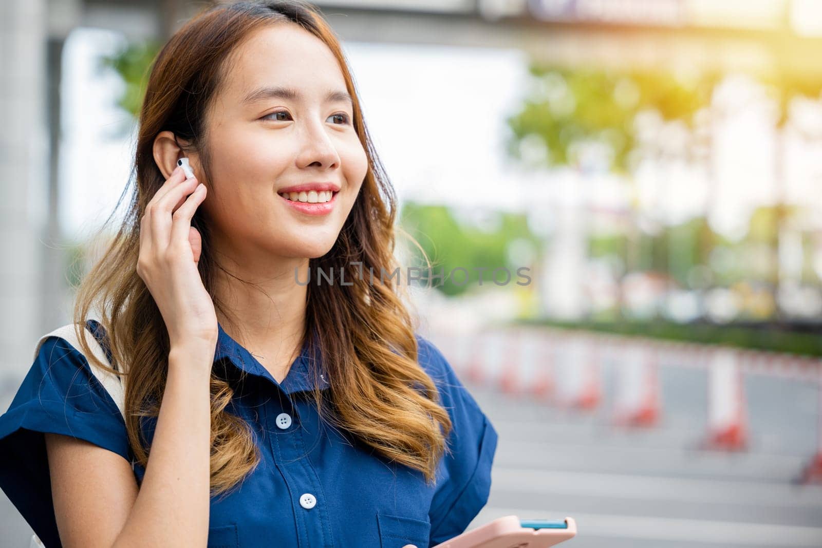 Smiling Asian girl using earbuds and smartphone for virtual chat and social media. This is a perfect portrait of a young person's lifestyle.