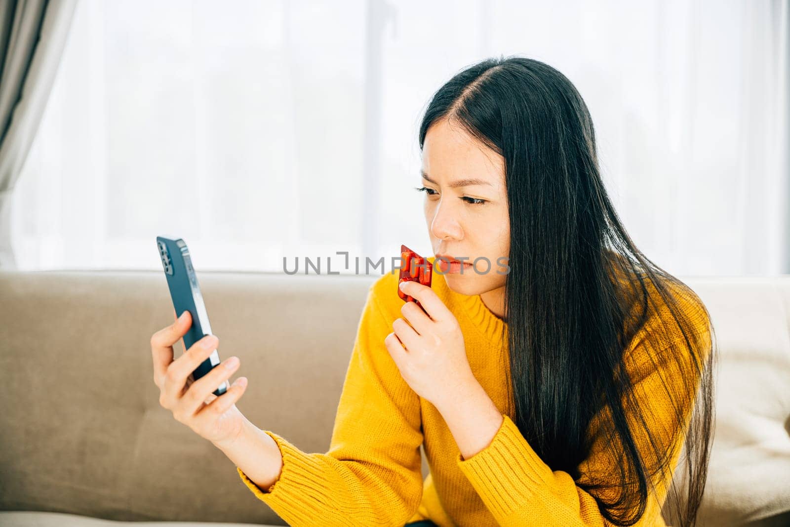 Depicting home consultation, Sick Asian woman on couch taking medicine consulting doctor via phone. Reflecting healthcare quarantine and social distancing during coronavirus.