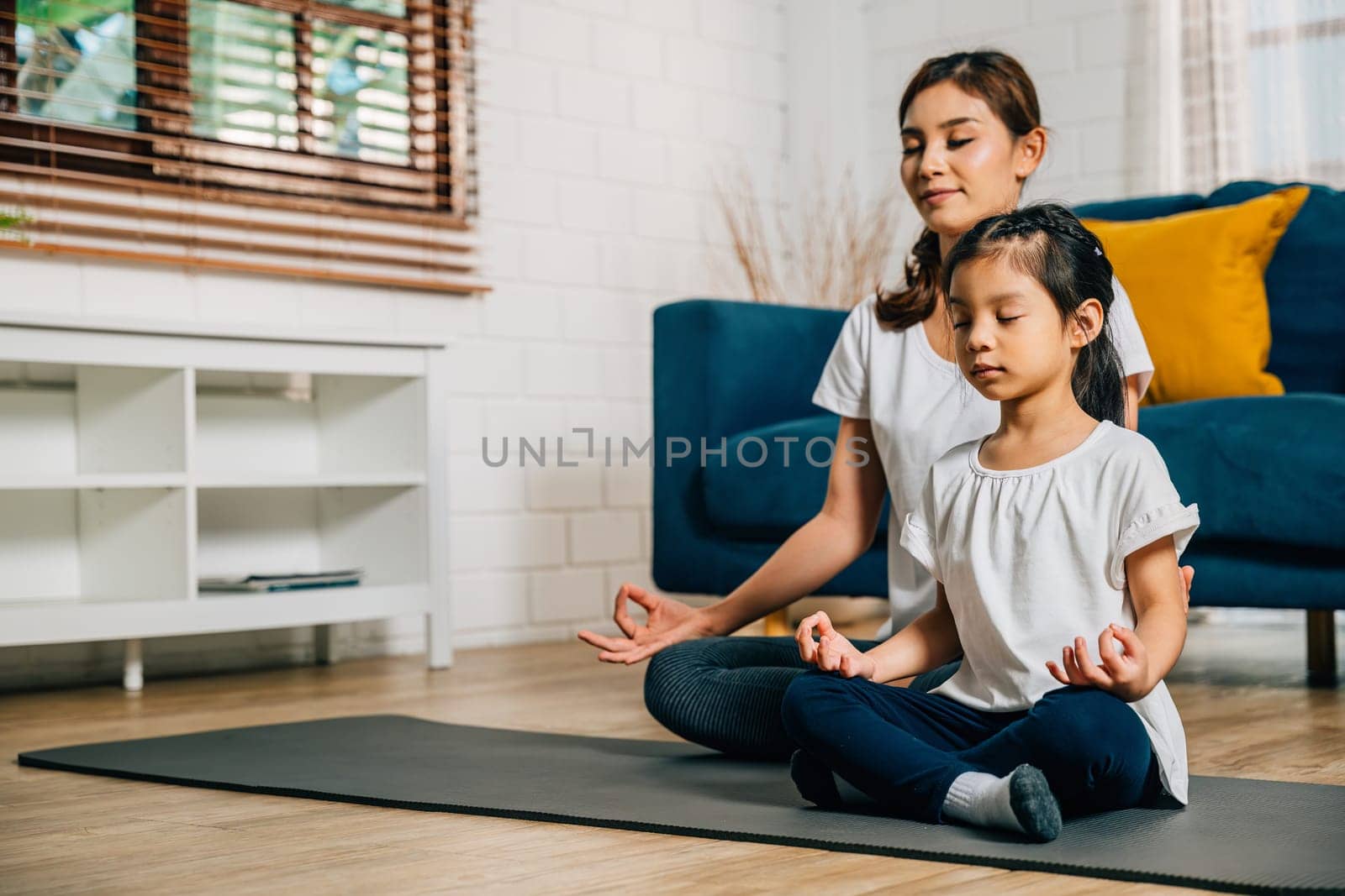 A mother and her daughter find serenity in family yoga sitting in lotus position by Sorapop