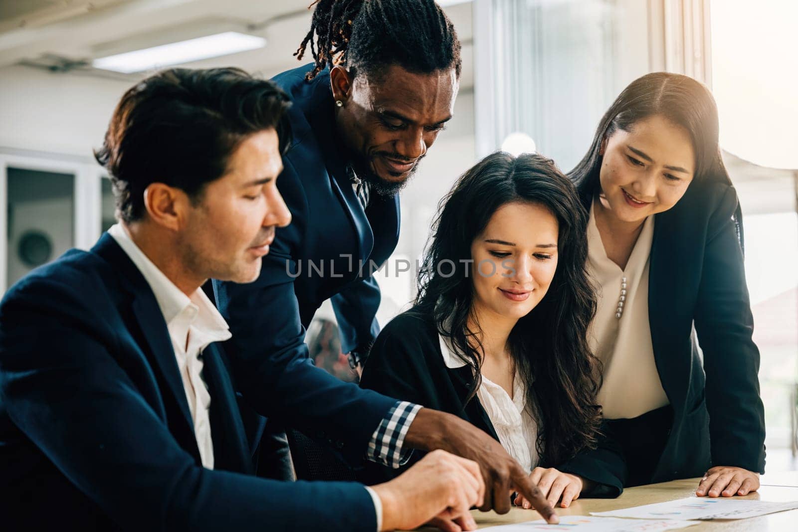 In a meeting room, a global team engages in lively discussion, led by a female leader. Together, they plan and collaborate on strategies, analyze charts, and work with documents for success.