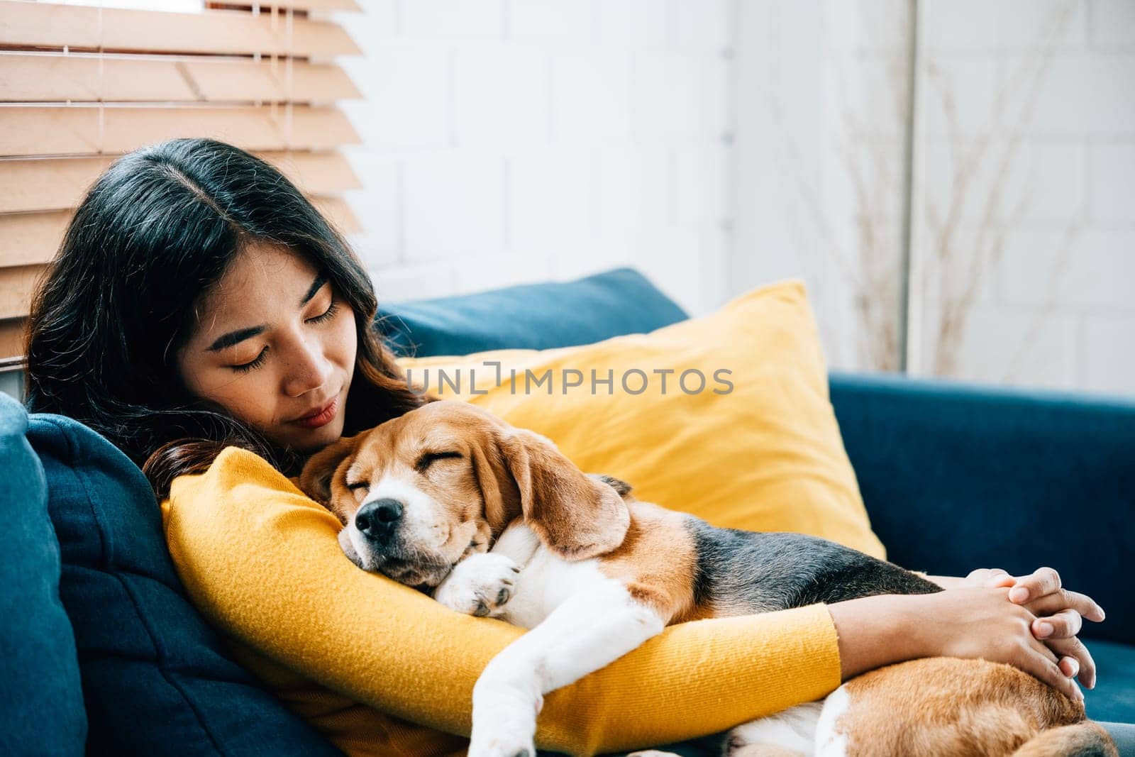 In the comfort of her home, a young Asian woman enjoys a peaceful nap on the sofa, sharing precious moments of trust, togetherness, and happiness with her beloved Beagle dog. Pet love by Sorapop