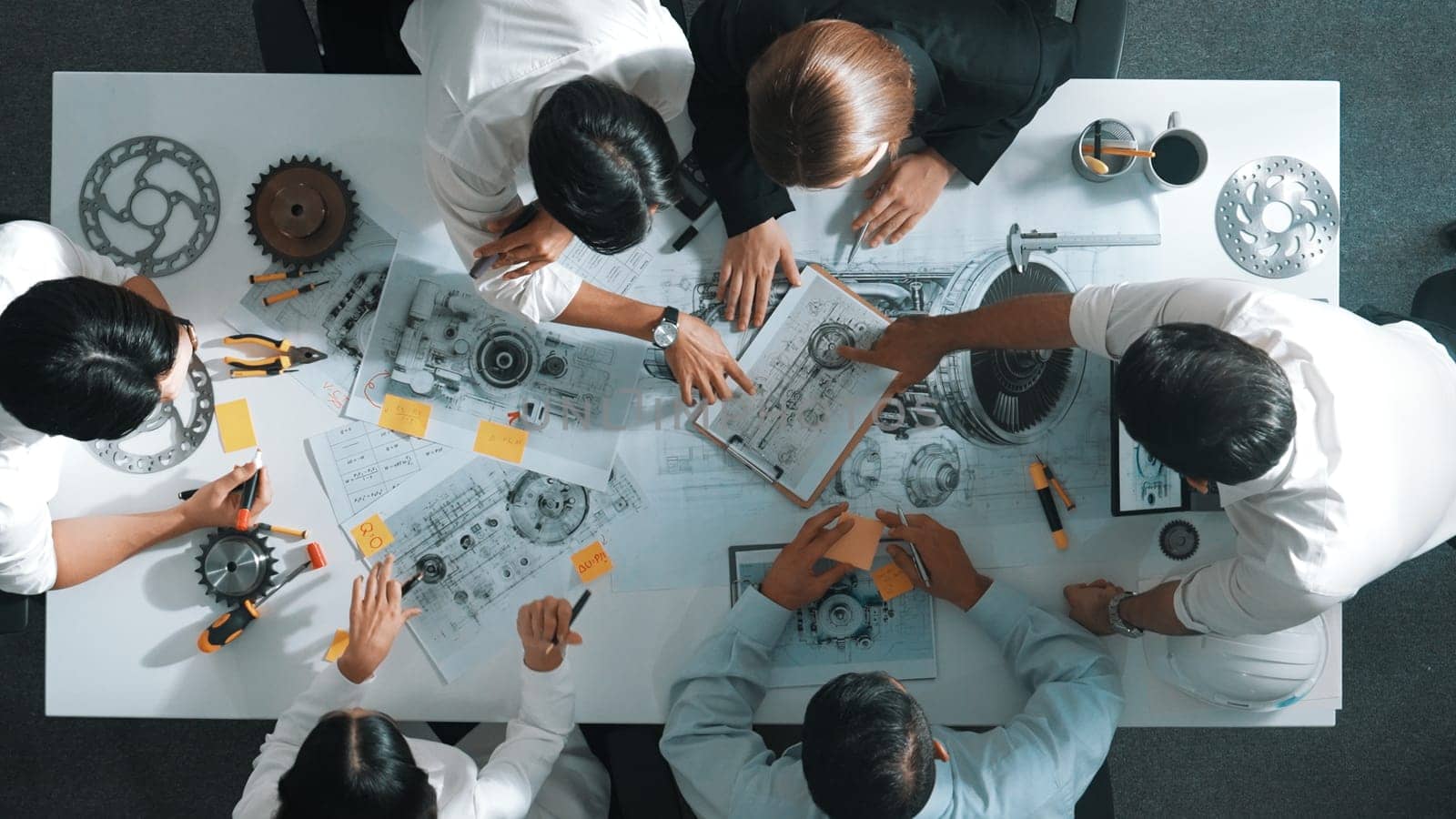 Top down aerial view of smart engineer team working together to design turbine engine. Professional technician discussing about jet engine construction while pointing at part of engine. Alimentation.