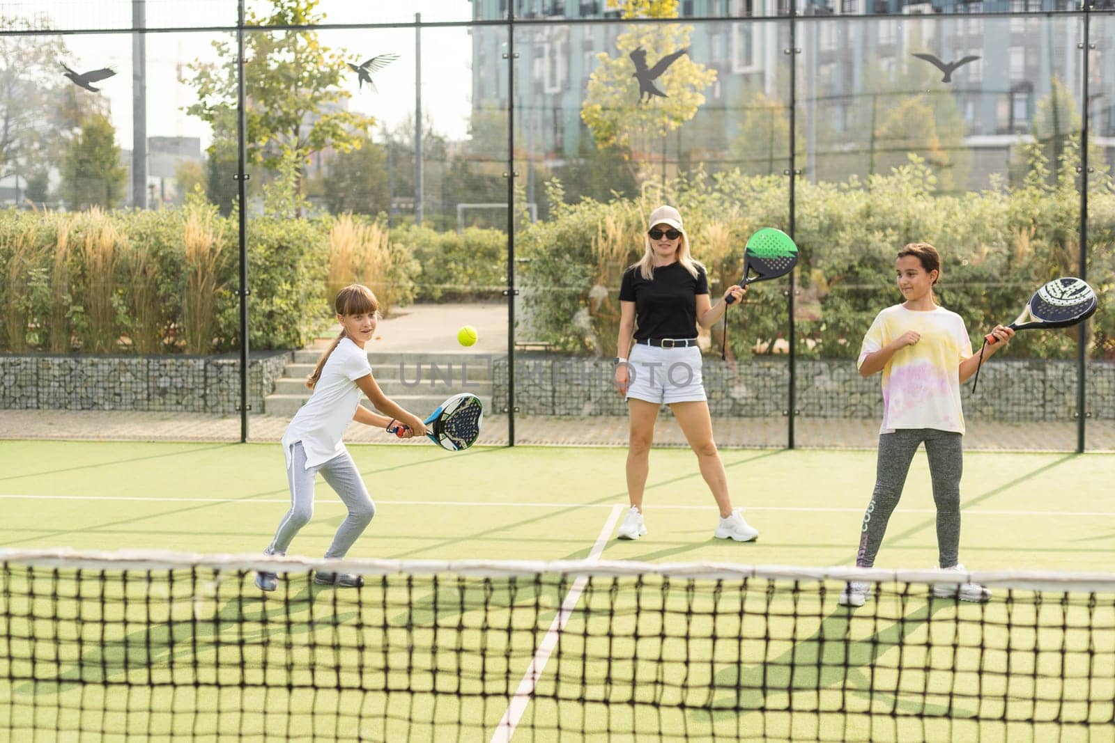 Cheerful coach teaching child to play tennis while both standing on tennis court by Andelov13