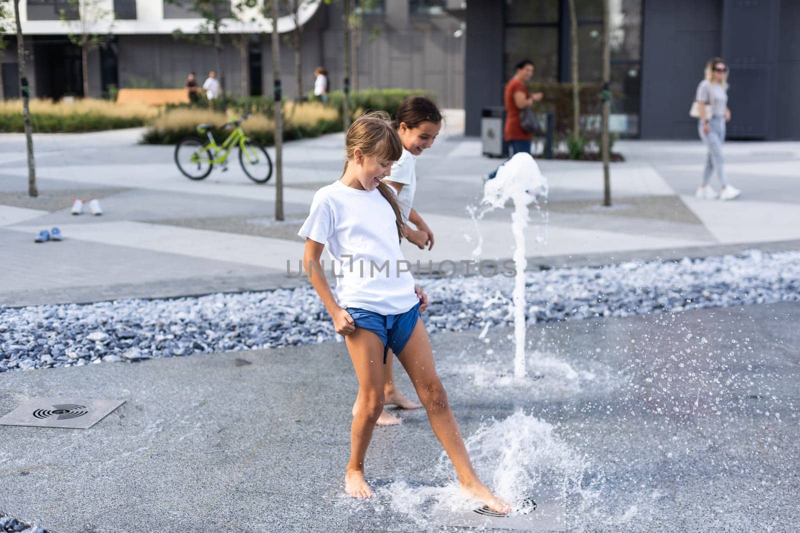 Cute young sisters playing in fountains. Children having fun with water on sunny summer day. Active leisure for kids. High quality photo