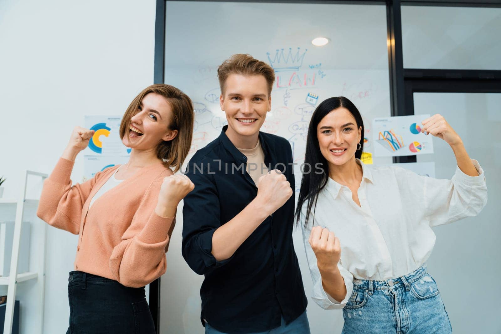 Successful caucasian business team posing victory pose to celebrate successful idea at creative business meeting in front of glass board. Unity and teamwork concept. Immaculate.